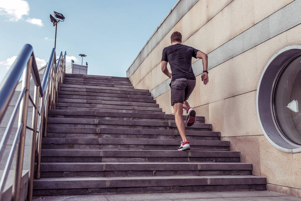 Athlete man runs in summer in city on steps, morning run, free space for text motivation fitness workout in fresh air. Jumping view from back. Sportswear shorts T-shirt Sneakers. - Fotoğraf, Görsel