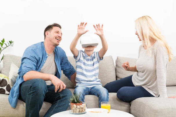 Famille heureuse à la maison sur le canapé du salon s'amuser à jouer à des jeux en utilisant un casque de réalité virtuelle
 - Photo, image