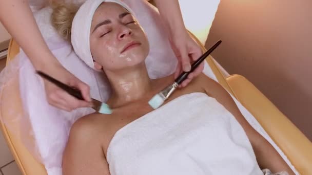 Professionele schoonheidsspecialiste aanbrengen masker met borstels op vrouw gezicht. - Video
