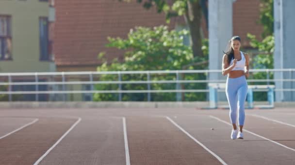 Beautiful Fitness Woman in Light Blue Athletic Top and Leggings Jogging in a Stadium. She is Running on a Warm Summer Afternoon. Athlete Doing Her Routine Sports Practice on a Track. Slow Motion. - Filmagem, Vídeo