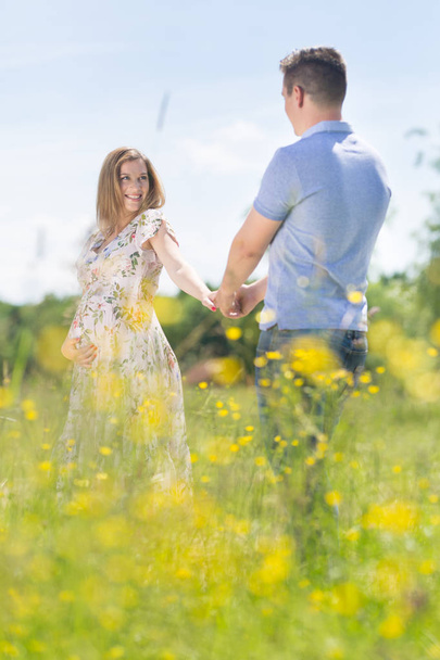 Young happy pregnant couple in love holding hands, relaxing in meadow. - Фото, зображення