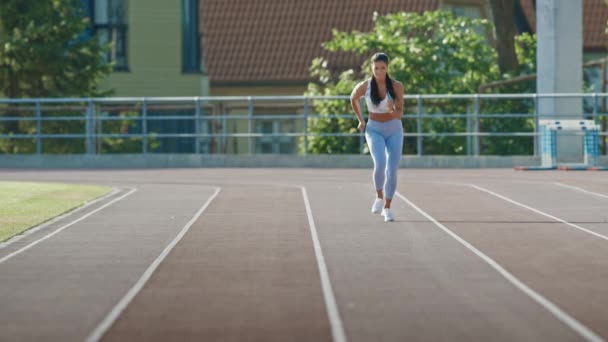 Beautiful Fitness Woman in Light Blue Athletic Top and Leggings is Starting a Sprint Run in an Outdoor Stadium. She is Running on a Warm Summer Day. Athlete Doing Her Sports Practice. - Filmmaterial, Video
