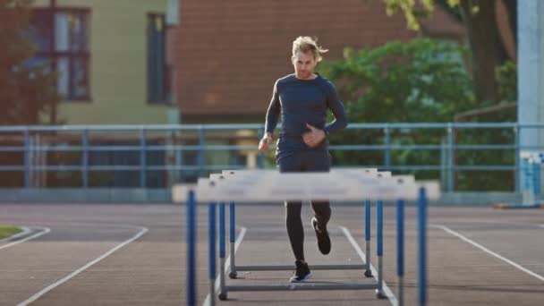 Athletic Fit Man in Grey Shirt and Shorts Hurdling in the Stadium. He is Jumping Over Barriers on a Warm Summer Afternoon. Athlete Doing His Routine Sports Practice. Slow Motion Tracking Shot. - Filmagem, Vídeo