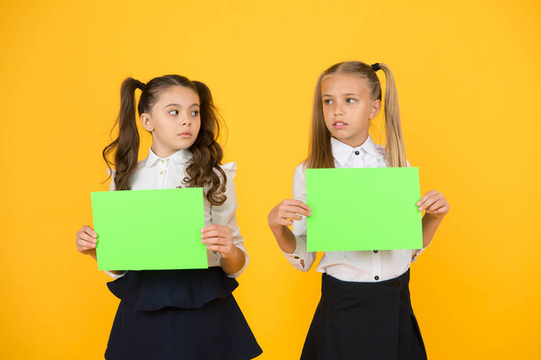 Thinking over a home work. Little children holding empty sheets for examination work on yellow background. Small girls with blank green papers for project work or research. Paper work, copy space - Zdjęcie, obraz
