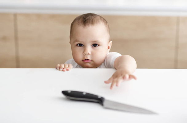 Μικρό αγοράκι που φθάνει στο χέρι για κοφτερό μαχαίρι στο τραπέζι της κουζίνας - Φωτογραφία, εικόνα