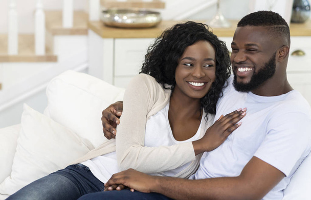 Ευτυχισμένο μαύρο ζευγάρι κάθεται στον καναπέ στο σπίτι, αγκαλιές - Φωτογραφία, εικόνα