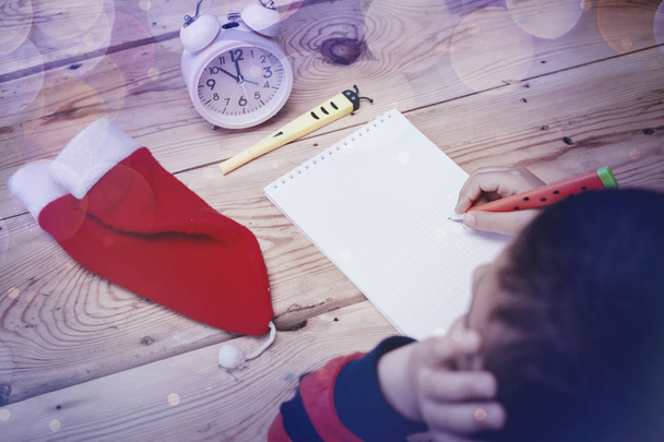 Маленький мальчик пишет Деду Морозу. Ребенок пишет письмо Санта Клаусу. Ребенок думает, мечтает о Рождестве
 - Фото, изображение