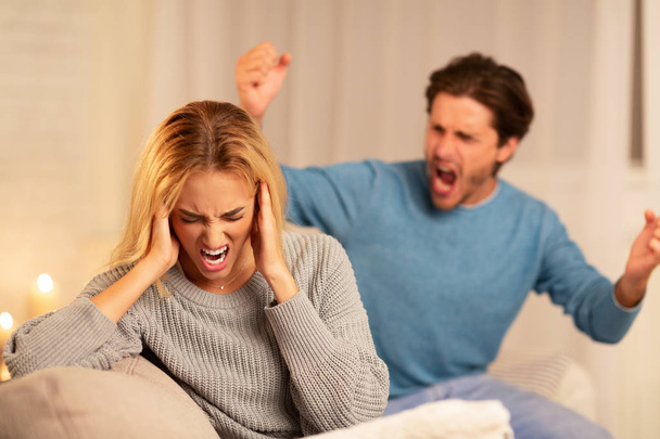 Marito abusivo che urla alla moglie seduta sul divano di casa
 - Foto, immagini