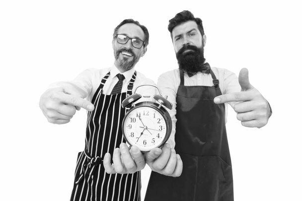 Time to cook. Men pointing at alarm clock. Man bearded hipster and mature chef apron white background. Cook dinner. We going to cook right now. Friends colleagues start cooking just on time - Photo, Image