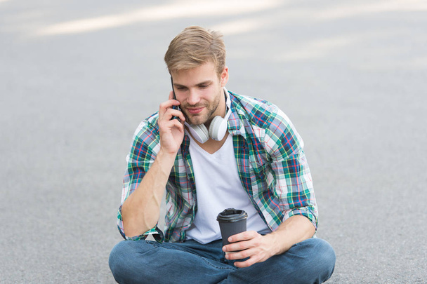 Morning vibes. man sit on ground. carefree student in headset. online education. listen music. man checkered shirt speak on phone. student relax and recharge. coffee to go. guy drink coffee - Φωτογραφία, εικόνα