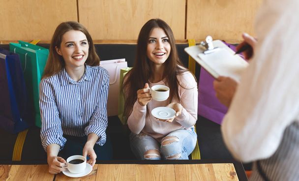 Две веселые девушки делают заказ в кафе и пьют кофе
 - Фото, изображение