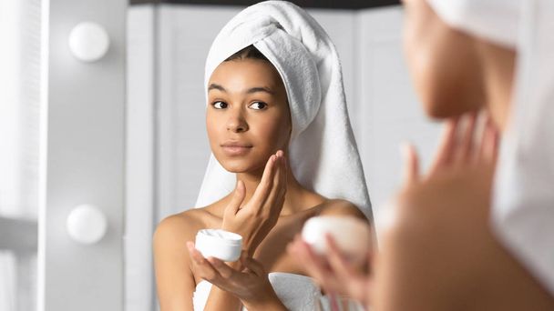 Девушка держит крем для лица продукт для увлажнения кожи в ванной комнате
 - Фото, изображение