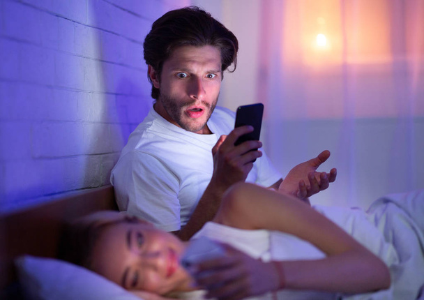 Man vangen vrouw chatten op telefoon in bed 's nachts - Foto, afbeelding
