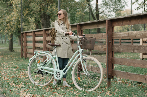 Woman holding rudder of her bike by a fence - Photo, image