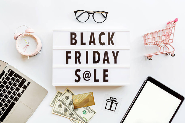 Creative promotion composition Black friday sale text on lightbox on white background, next grocery trolley, credit card, cash money, mobile phone, shopping bag. Flat lay, top view, overhead, mockup - Fotografie, Obrázek