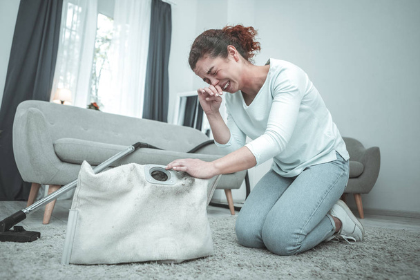 Ama de casa sentada en el suelo y estornudos con alergia al polvo
 - Foto, Imagen