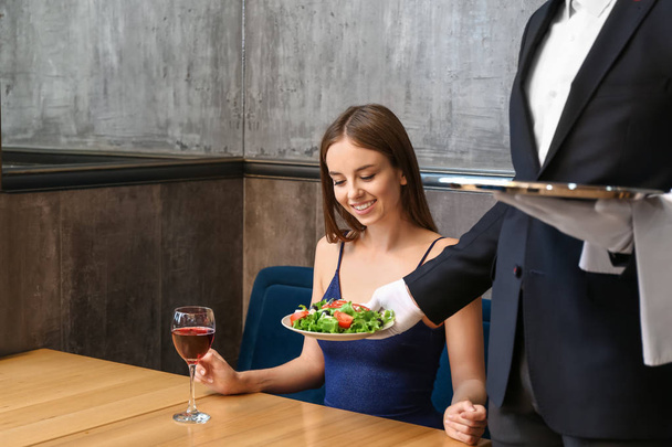 Camarero trayendo ensalada para mujer joven en restaurante
 - Foto, Imagen