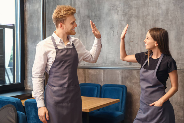 Young waiters giving high-five to each other in restaurant - 写真・画像