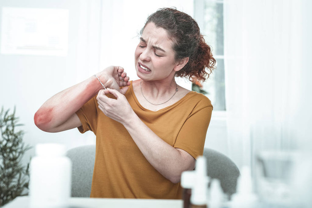 Curly woman taking bracelet off while having rash on wrist - Photo, image