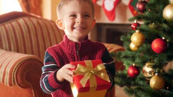 4k video of happy smiling little boy holding Christmas gift in box and showing his present in camera. Child receiving gifts and presents from Santa Claus on winter holidays and celebrations - Filmmaterial, Video