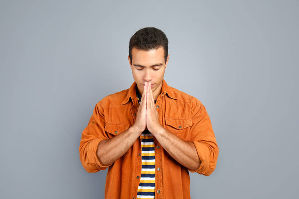 Jonge Afro-Amerikaanse man bidden op grijze achtergrond - Foto, afbeelding