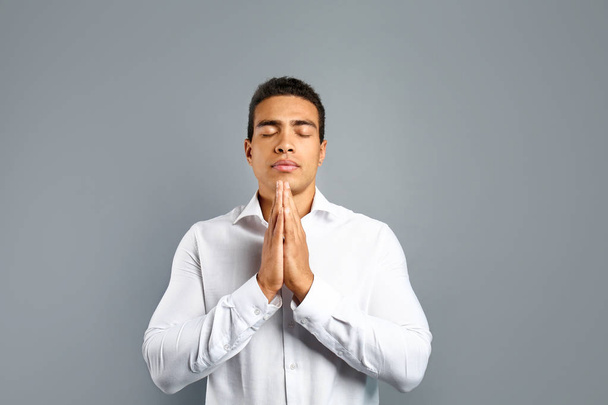 A szürke háttéren imádkozott fiatal afro-amerikai férfi - Fotó, kép