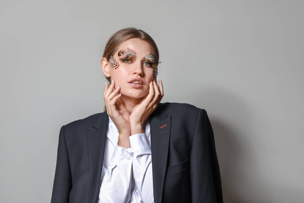 Mujer joven con pestañas y cejas creativas sobre fondo gris
 - Foto, Imagen