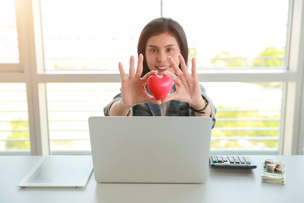 businesswoman holding red heart symbol on table with computer - Foto, afbeelding