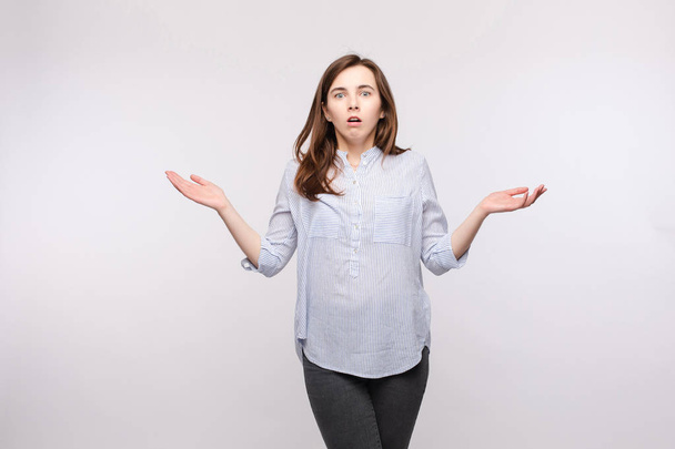 Brunette woman showing puzzled reaction.Studio portrait of brunette woman in casual clothes showing puzzlement or confusion and reacting with her arms up in amazement. - Photo, Image