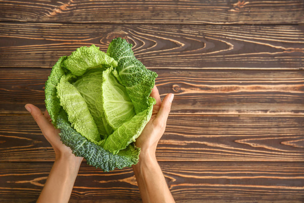 Female hands with fresh savoy cabbage on wooden background, top view - Photo, Image