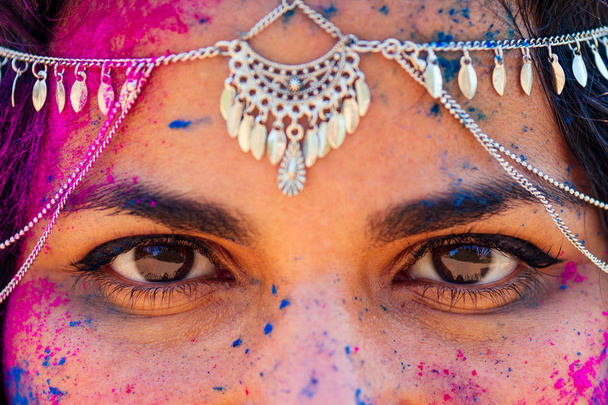 young Indian face in paint Woman in traditional indian pink outfit with jeweler celebrating Holi color festival.girl with black hair with bindi on the head snow-white smile.Brown eyes oriental female - Фото, изображение