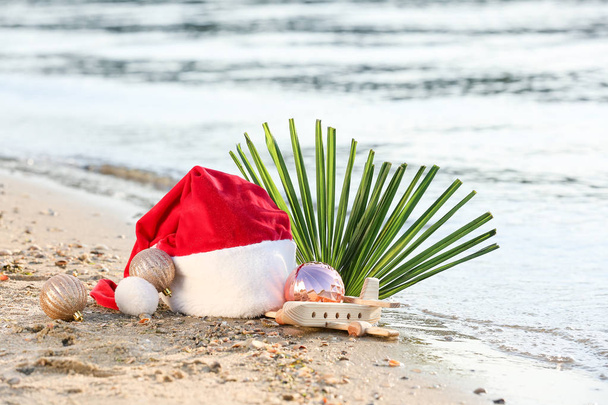 Шляпа Санта-Клауса с деревянным самолетом и мячами на морском побережье. Рождественские каникулы
 - Фото, изображение