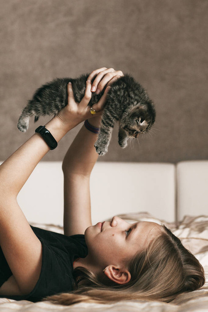 Lapsi makaa sängyllä ja leikkii brittiläisen kissanpennun kanssa.
 - Valokuva, kuva