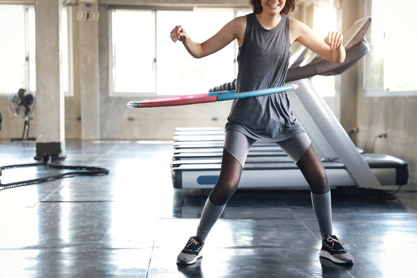 καλό σχήμα της γυναίκας στο άθλημα φορούν άσκηση στο Χούλα Χουπ στο γυμναστήριο με χαρούμενο χαμόγελο πρόσωπο - Φωτογραφία, εικόνα