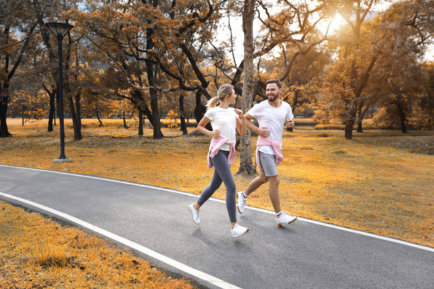 junges und gesundes Paar, das im Herbst im Park joggt (gesundes oder valentinisches Konzept)) - Foto, Bild