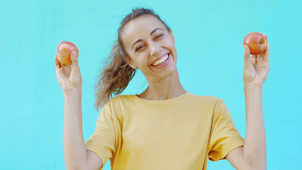 Menina muito sorridente está posando em um fundo ciano brilhante colorido, e mostra maçãs amarelas-vermelhas maduras frescas saborosas. mulher mostra felicidade, prazer e emoções positivas
 - Filmagem, Vídeo