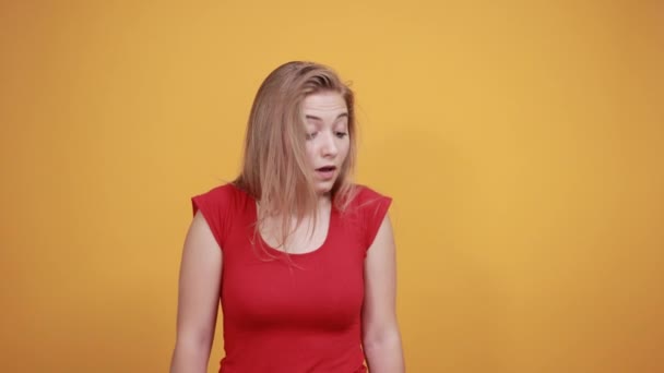 молодая блондинка в красной футболке на изолированном оранжевом фоне показывает эмоции
 - Кадры, видео