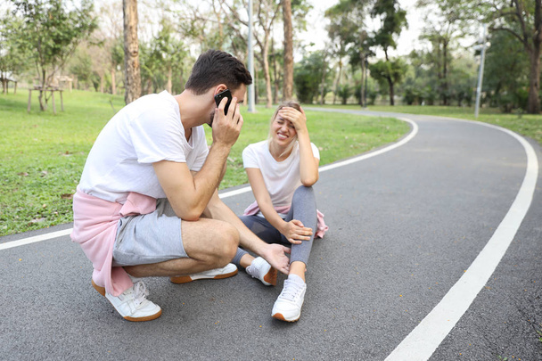 young girl fall down because of the dizziness from too much exercise and young man is helping by using cell phone calling someone  - Foto, Imagen