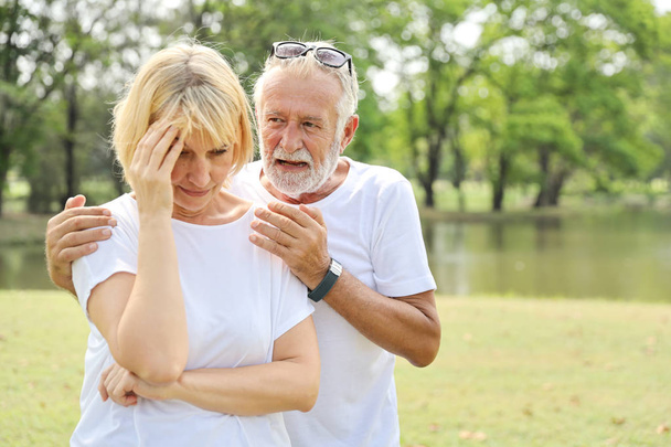 літній чоловік втішає дружину і кладе руки їй на плече з любов'ю в парку з зеленим деревом в літній час
 - Фото, зображення