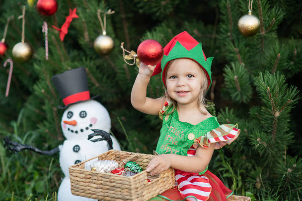 A gyerek karácsonyra vár Juliban. portré egy kislányról a karácsonyfa mellett. Baba díszítő karácsonyfa. téli ünnepek és az emberek koncepciója. Boldog karácsonyt és boldog ünnepeket!. - Fotó, kép
