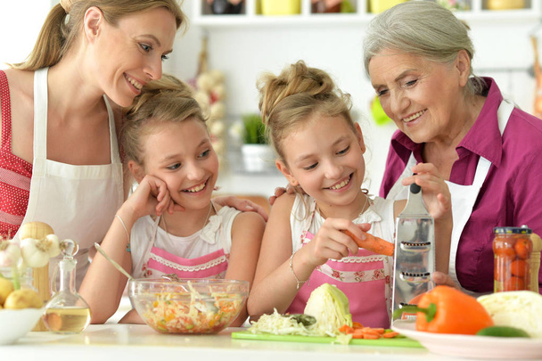 Cute girls with mother  preparing delicious fresh salad in kitchen - Fotó, kép