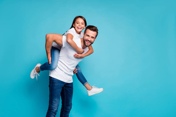 Portrait of cheerful people laughing piggyback wearing white t-shirt denim jeans isolated over blue background - 写真・画像