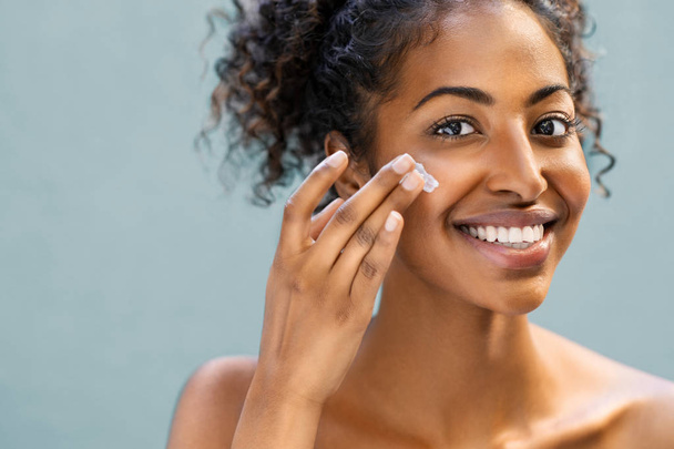 Woman applying moisturizer on face - Фото, изображение