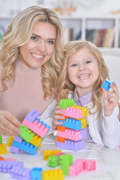  little girl and her mother playing with colorful plastic blocks at home - Foto, afbeelding