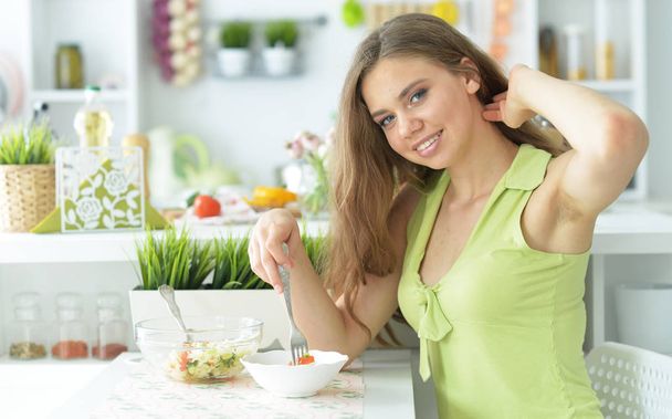 cute girl eating salad  on kitchen - Foto, afbeelding