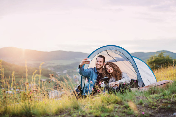 Young tourist couple travellers with tent shelter sitting in nature, taking selfie. - Foto, immagini