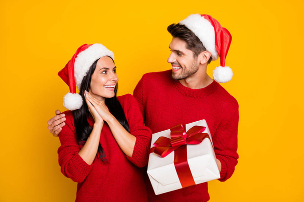 Portrait of handsome man in xmas hat give package to his impressed wife wear red pullover isolated over yellow background - Valokuva, kuva