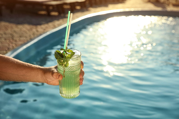 Man with glass of fresh summer cocktail near swimming pool outdoors, closeup. Space for text - Photo, Image