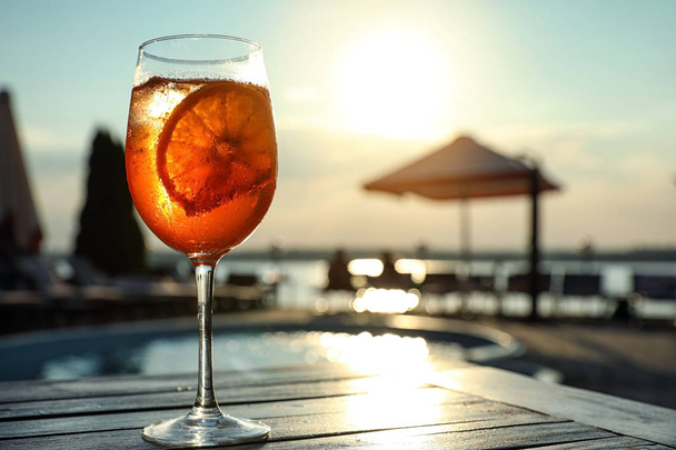 Glass of fresh summer cocktail on wooden table near swimming pool outdoors at sunset. Space for text - Φωτογραφία, εικόνα