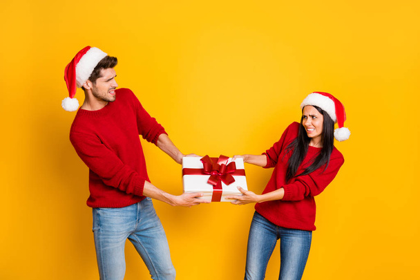 Profile side of angry couple pull package wear red sweater pullover santa claus cap denim jeans isolated over yellow background - Photo, Image